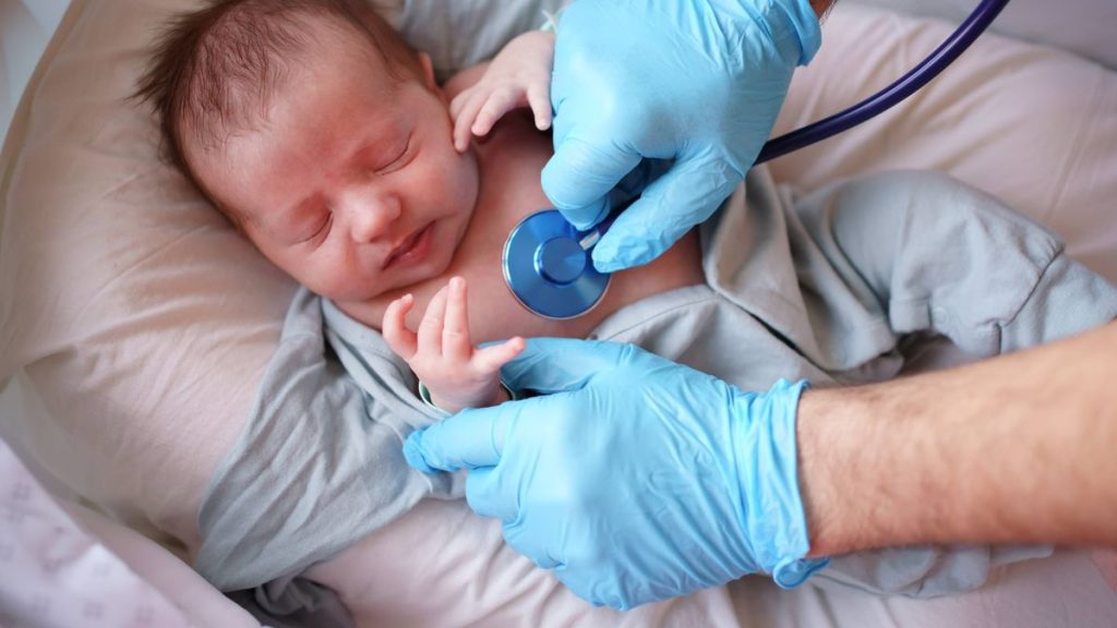 0 Male in blue medical gloves uses a stethoscope as he listens closely to a baby