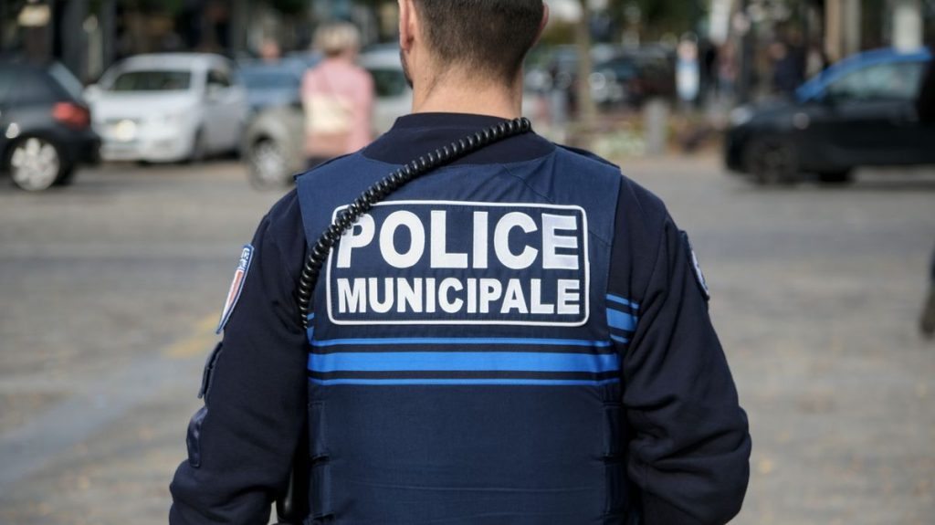1 A municipal police officer seen from behind wearing a blue uniform and radio equipment while standin